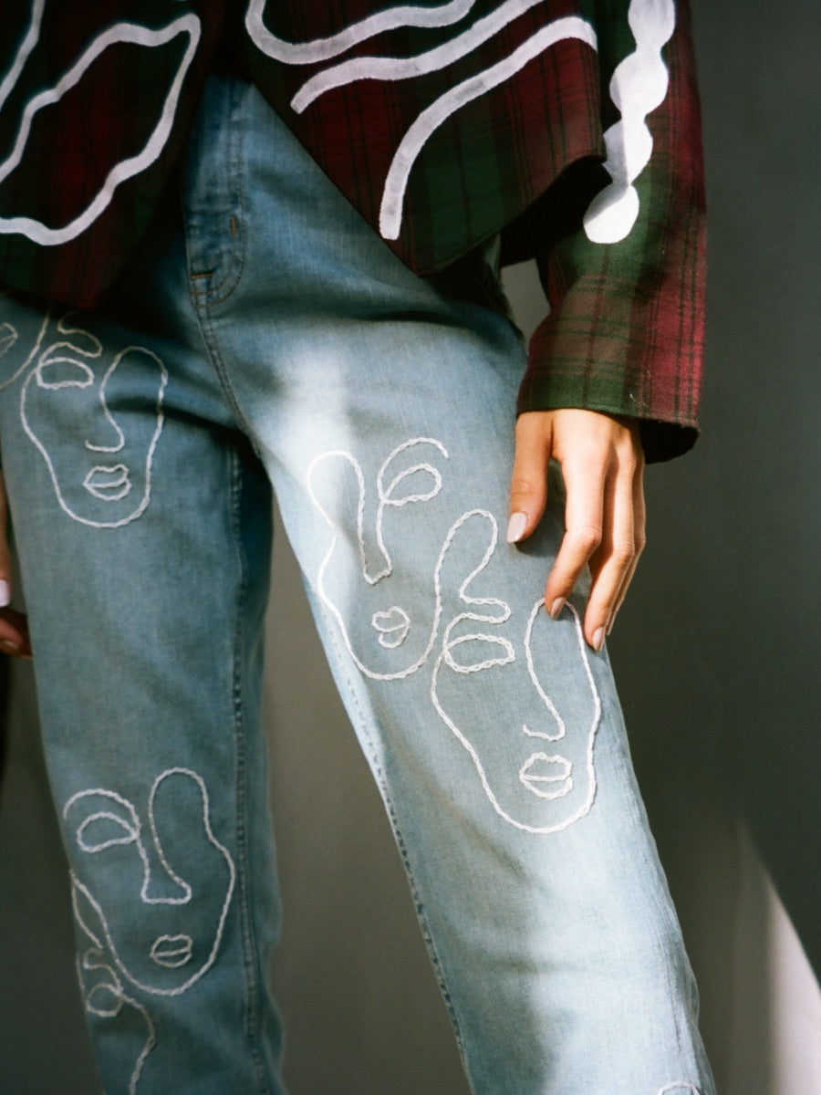 Fanfare Label sustainable women’s clothing brand UK. Our upcycled jeans are high-waisted, blue denim and made from recycled denim. We decorate every jean with a white embroidered thread in a face design.