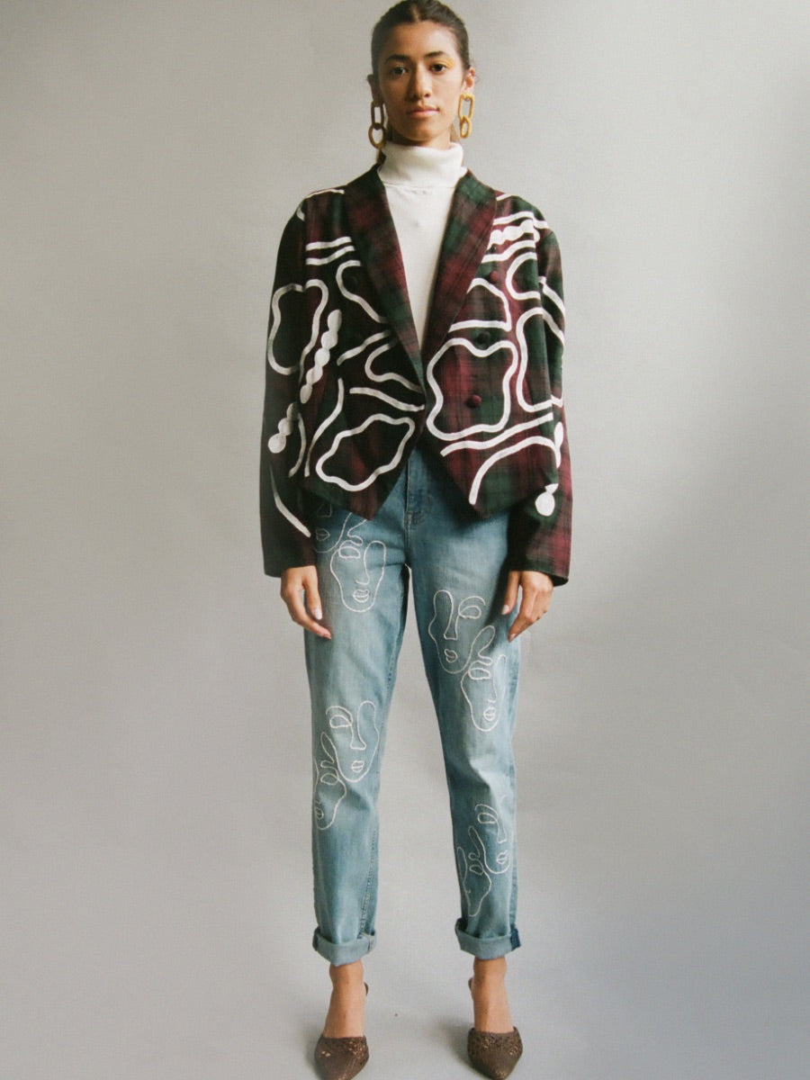 Fanfare Label sustainable women’s clothing brand UK. Our upcycled jeans are high-waisted, blue denim and made from recycled denim. We decorate every jean with a white embroidered thread in a face design.