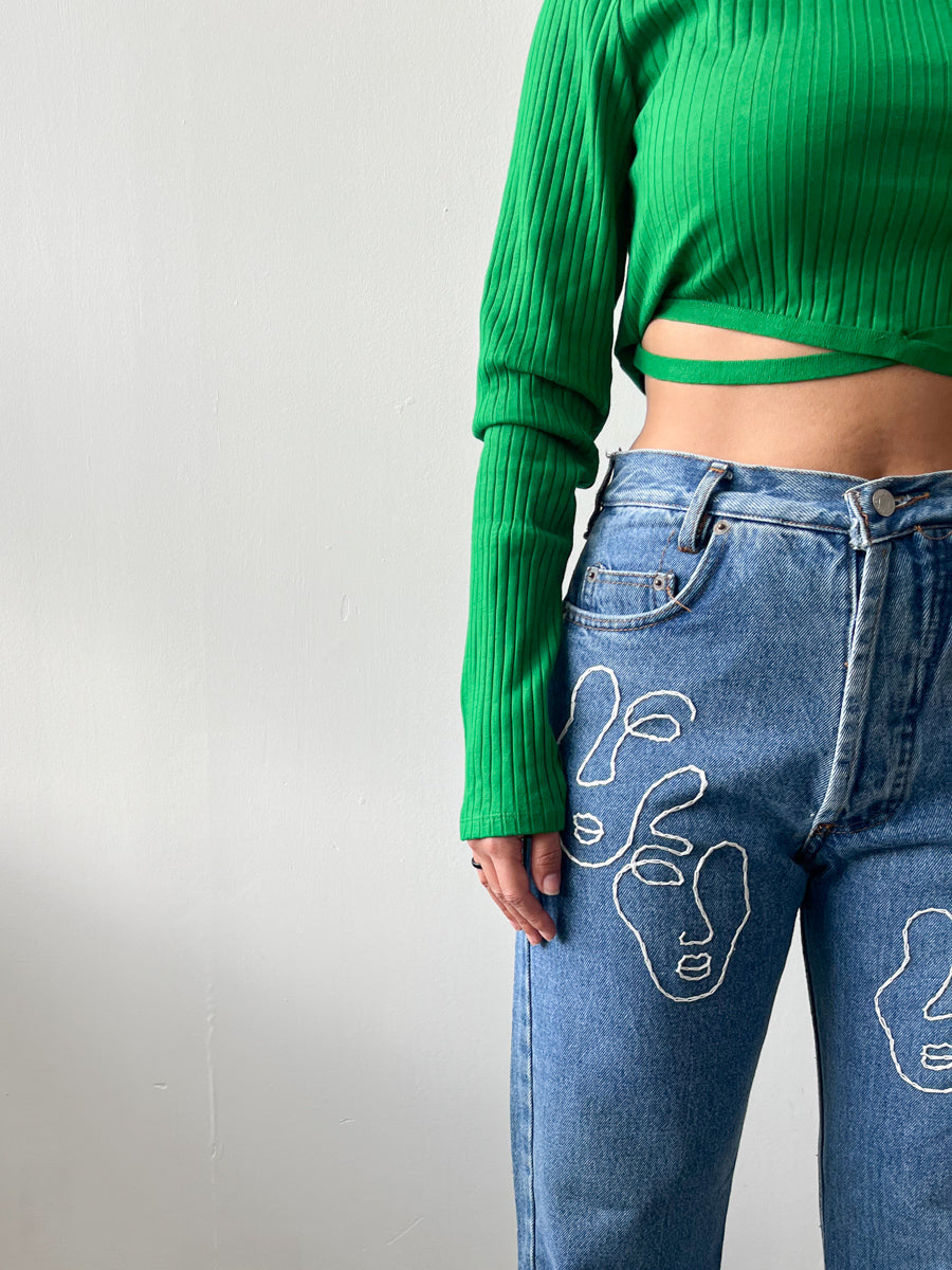 Fanfare Label sustainable women’s clothing brand UK. Our upcycled jeans are high-waisted, blue denim and made from recycled denim. We decorate every jean with a white embroidered thread in a face design.