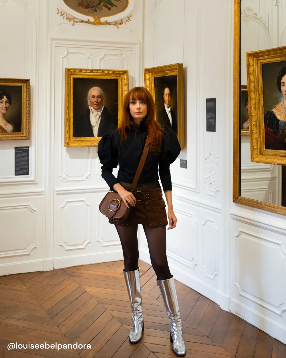 Louise porte les bottes CRISTOBAL à talon en cuir argent avec un short et une blouse noire
