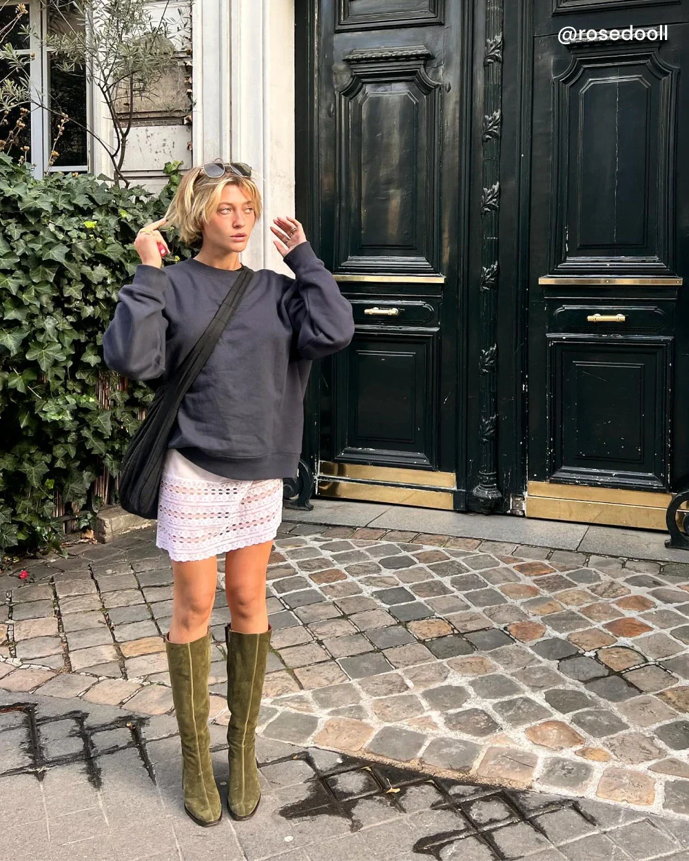 Rose porte les bottes CRISTOBAL à talon en daim kaki avec une jupe blanche et un pull